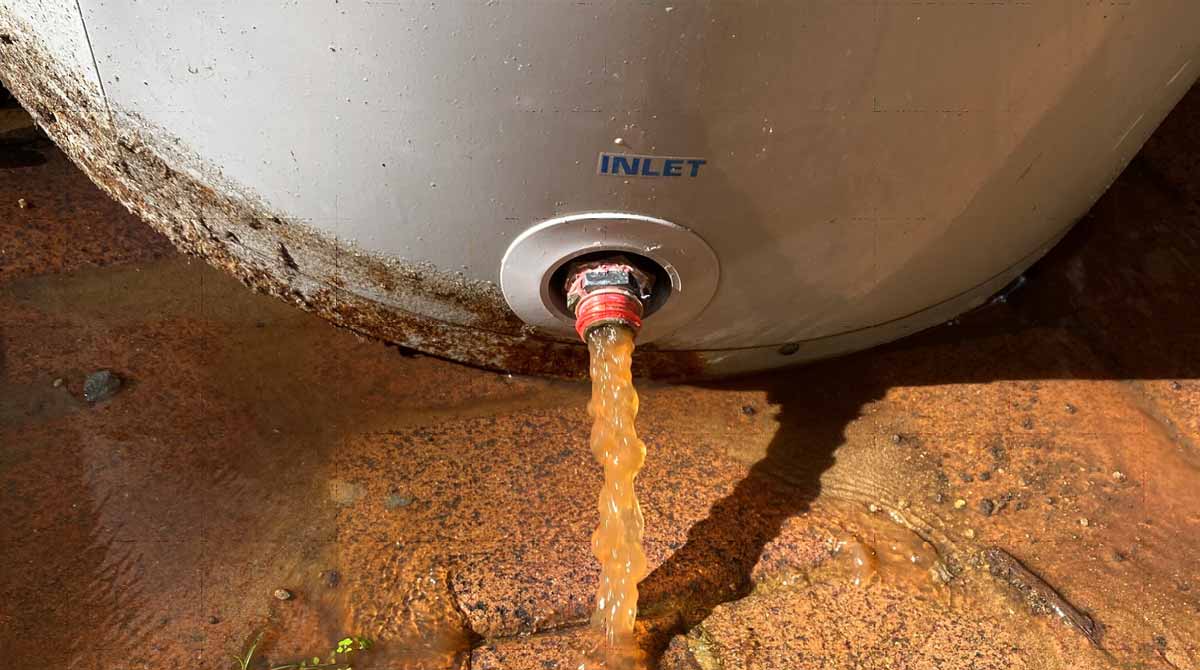 Rust-colored contaminated water pouring from a household hot water tank inlet